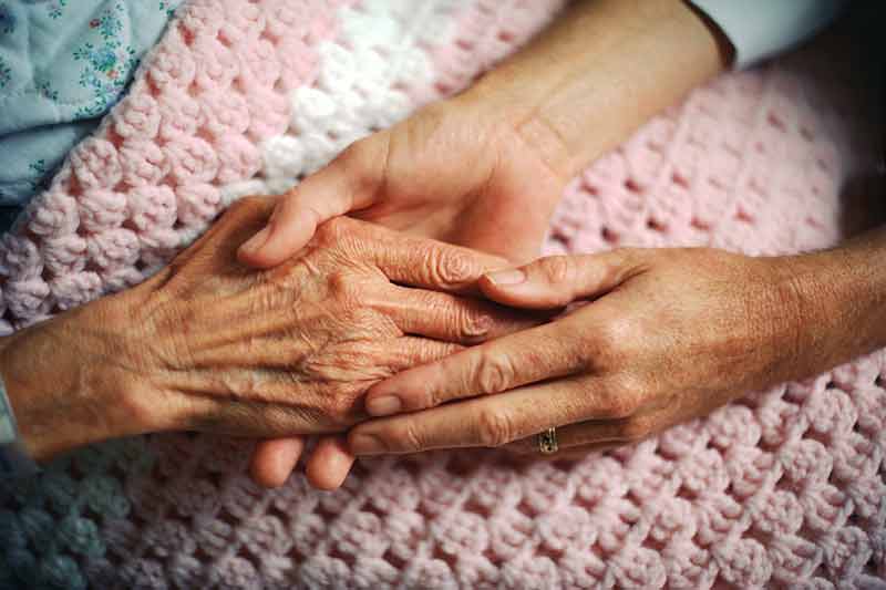 A caregiver gently holds an elderly person’s hands.