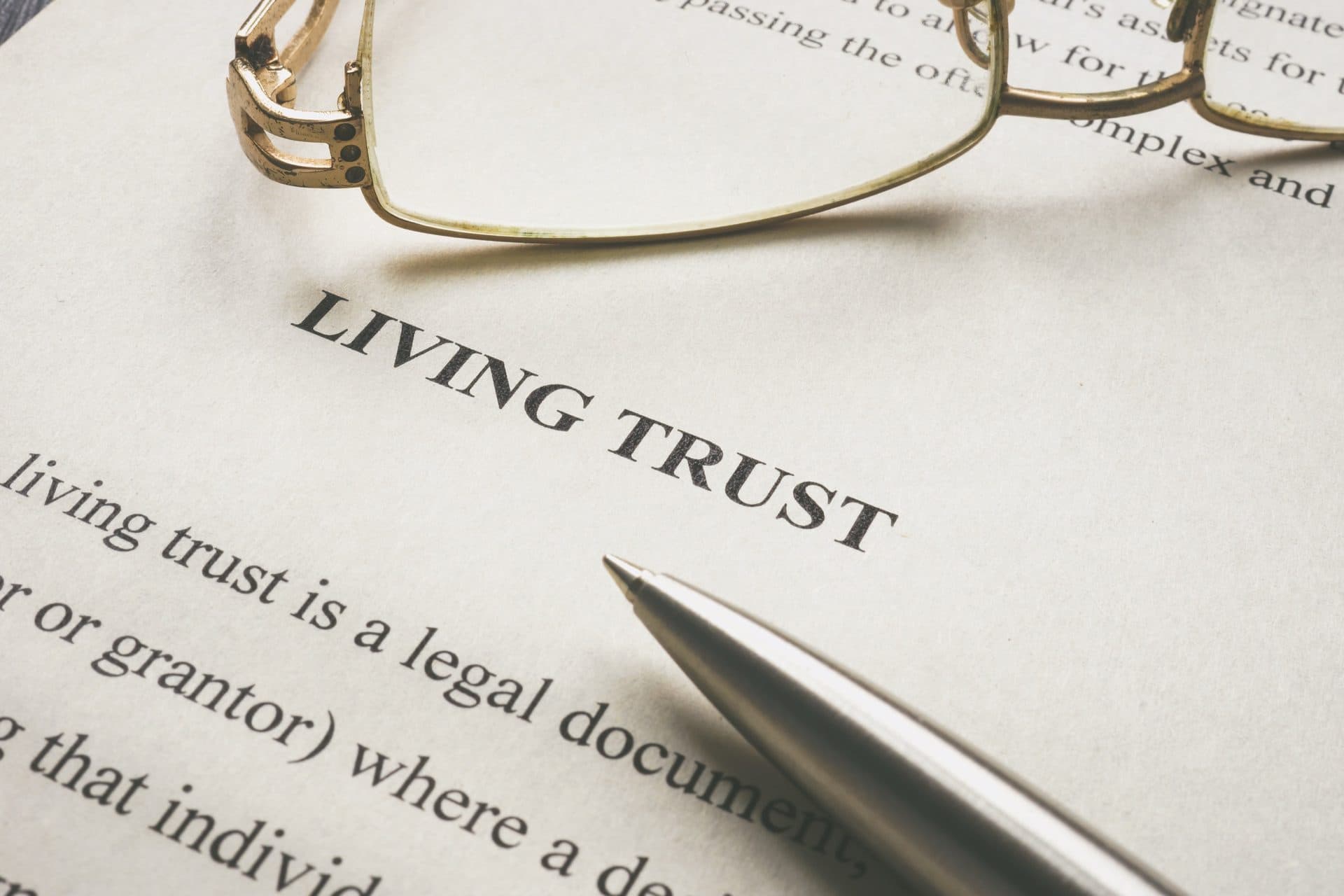 A printed Living Trust legal document with a silver pen and a pair of gold reading glasses resting on top, illustrating the paper documents that make up a California estate plan.