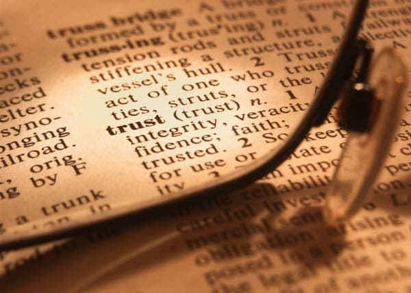 Dictionary close-up of the word trust beneath reading glasses.
